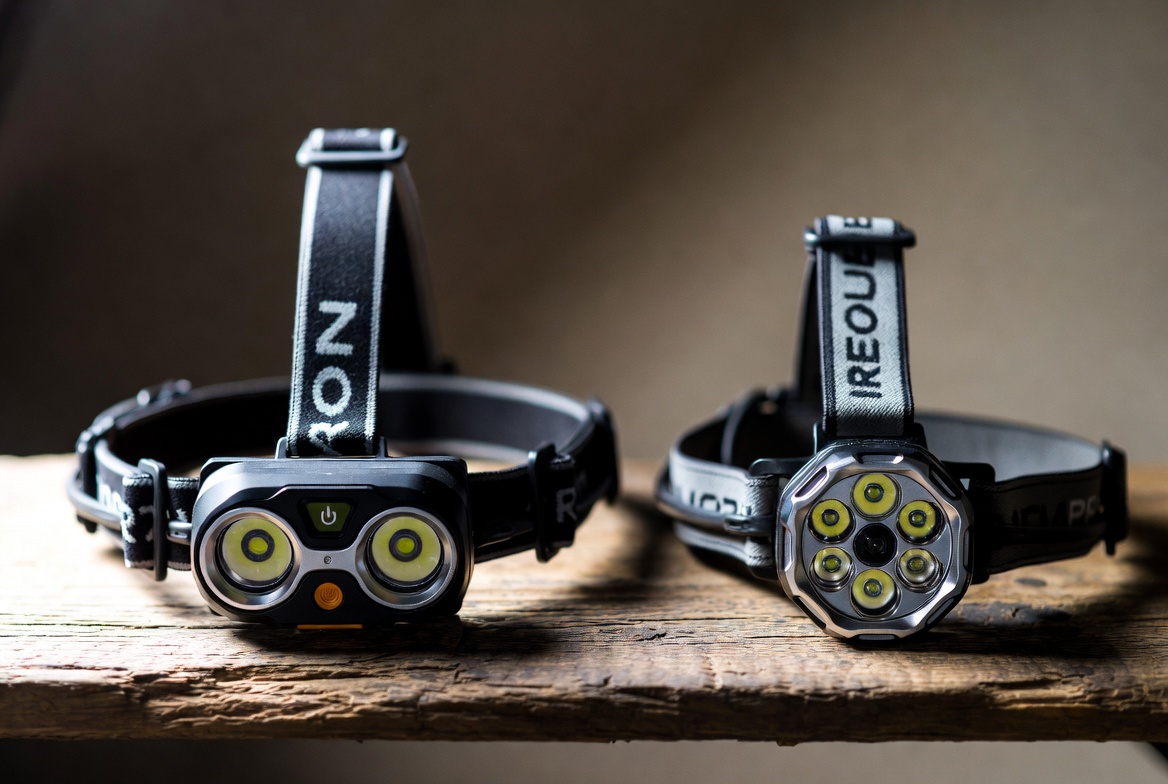 Two rechargeable headlamps side by side on a wooden table with straps visible